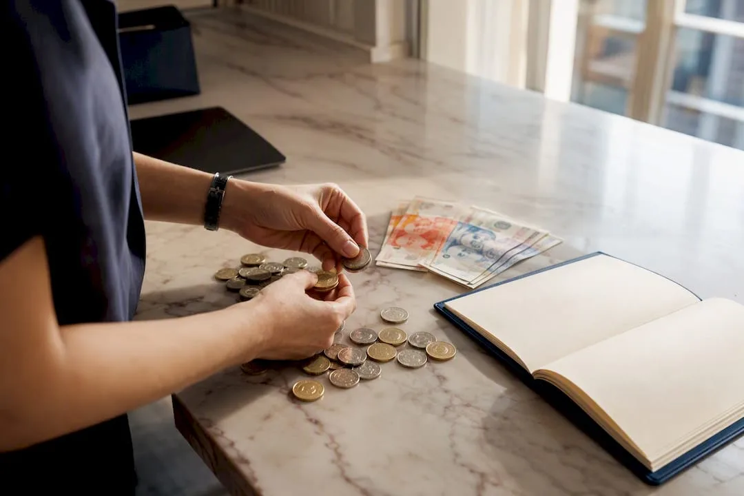 Hands counting coins and calculator on desk